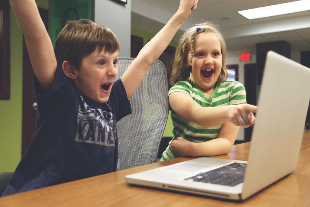 Crianças felizes em frente a um notebook. A imagem ilustra post sobre os 4 pilares da educação.