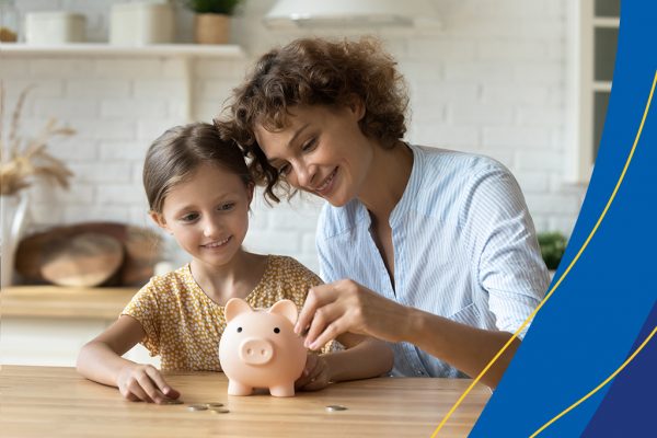 Mãe e filha com um cofre de porquinho na frente e algumas moedinhas pela mesa. A imagem ilustra um post sobre educação financeira nas escolas.